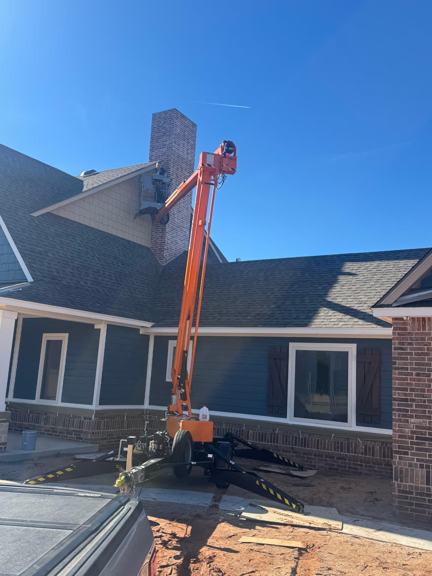 painter in a lift painting trim and fascia beside a brick chimney in Oklahoma